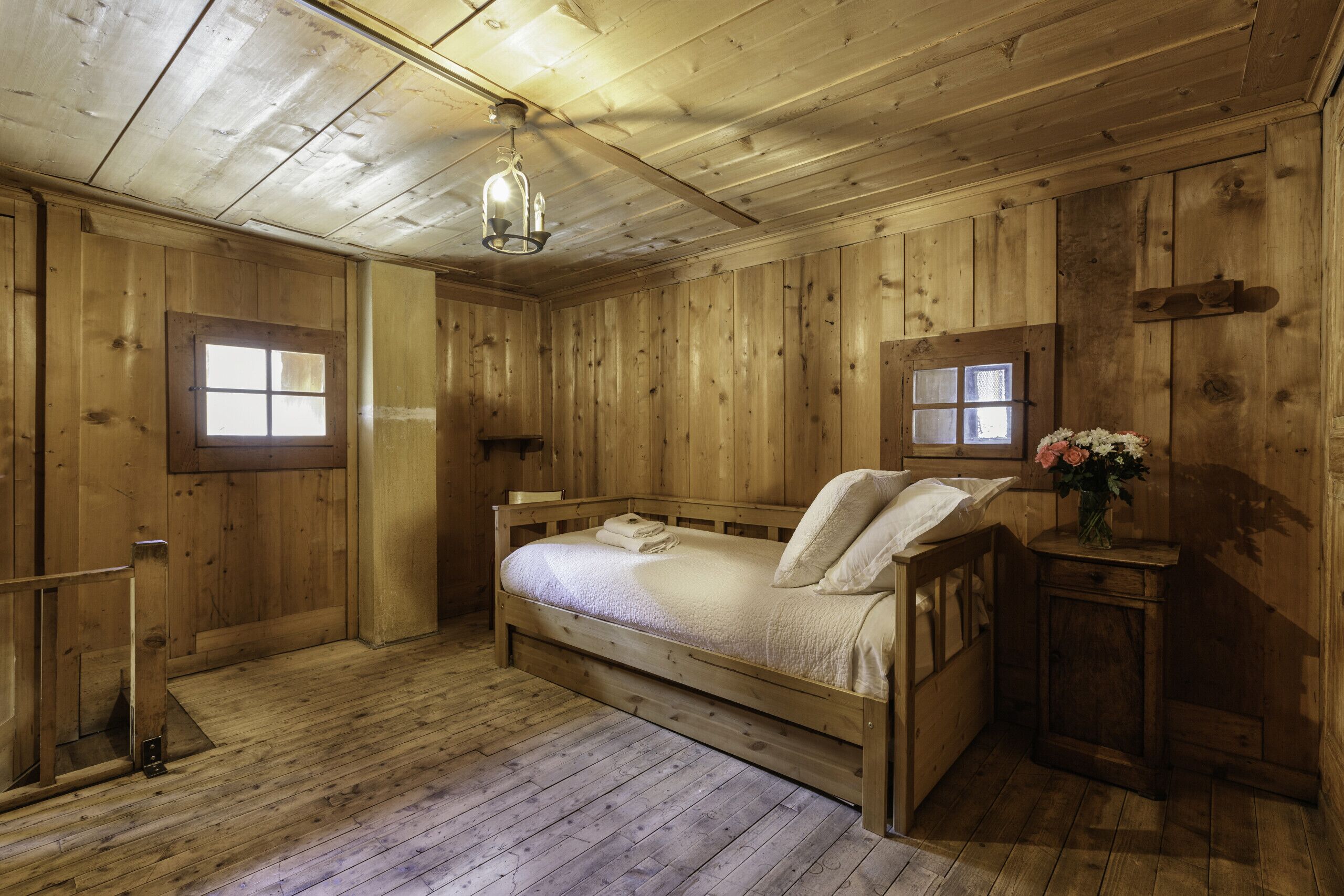 A wooden cabin room with a bed, a small table, and a window.