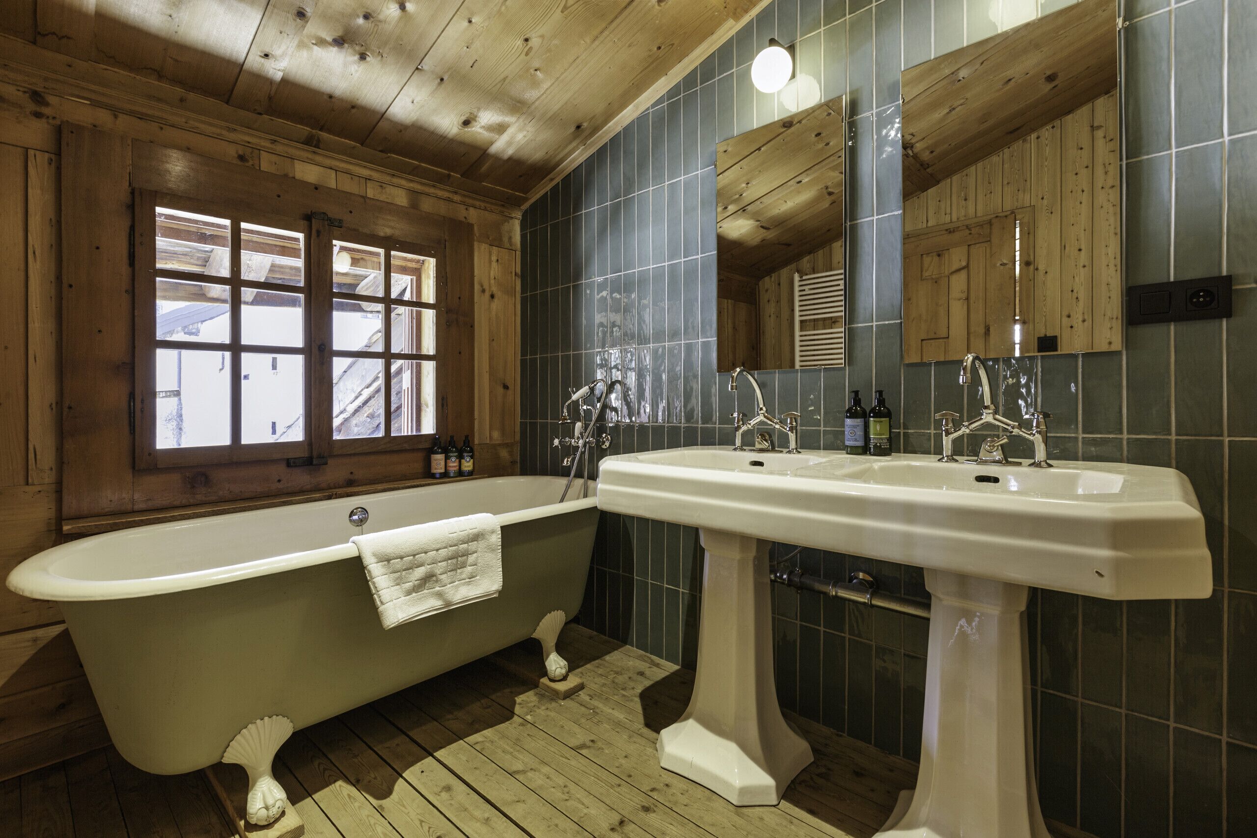 A bathroom with a freestanding bathtub, a pedestal sink, and a window with a view.