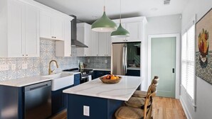 A modern kitchen with white cabinets, a marble island, and a green pendant light. - Zen Den (Atlanta)