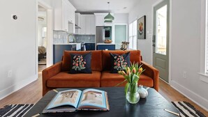 A modern living room with a sofa, a coffee table with a book, and a vase with flowers. - Zen Den (Atlanta)