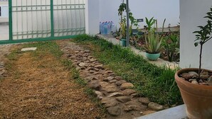Un patio con un área de estar techada, un pequeño jardín con plantas en macetas y un camino empedrado.