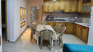 Una cocina compacta con armarios de madera, un televisor integrado, una mesa de comedor con sillas y un refrigerador pequeño.