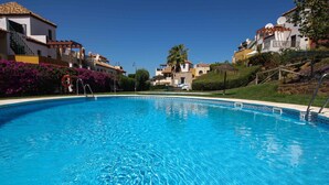 A clear blue swimming pool surrounded by buildings with balconies and satellite dishes, under a clear sky.