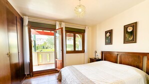 A bedroom with a bed, a nightstand, a lamp, a window, and a door leading to a balcony.