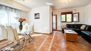 A spacious living room with a glass coffee table, a black leather sofa, and a white dining set.