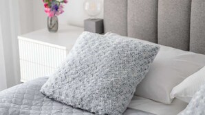 Una cama bien hecha con un edredón blanco y un almohadón mullido.