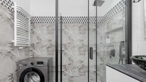 Un lavadero pequeño con lavadora, cabina de ducha de vidrio y pared con estampado.