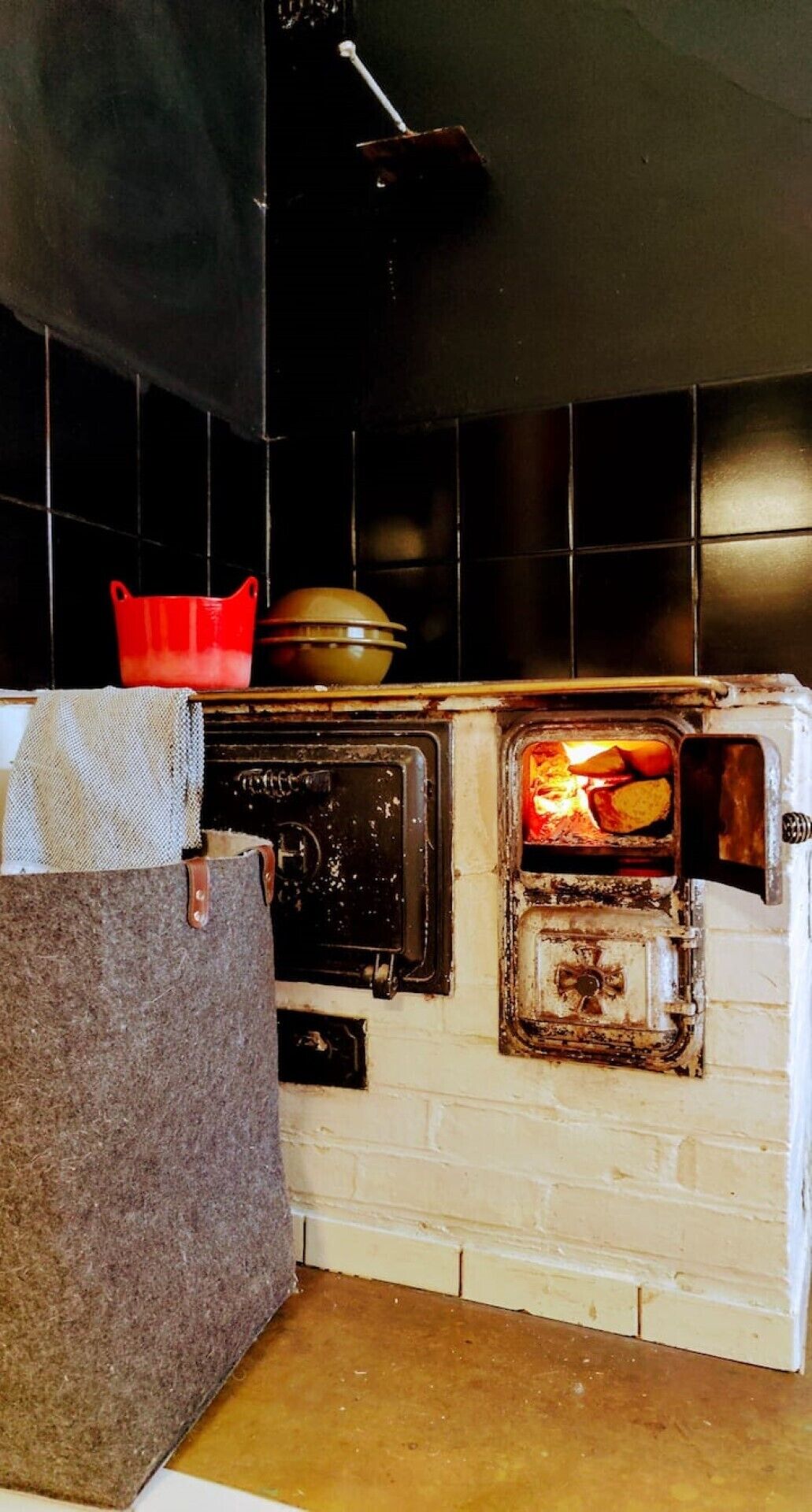 Une cuisine avec un mur en briques, une cuisinière et une casserole rouge posée sur le plan de travail.