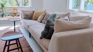 Un salon moderne avec un canapé beige, des coussins à motifs, une petite table ronde et un tapis marron.