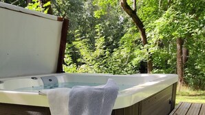 Un bain à remous avec une serviette blanche et une serviette rayée, le tout installé sur une terrasse en bois entourée de verdure.