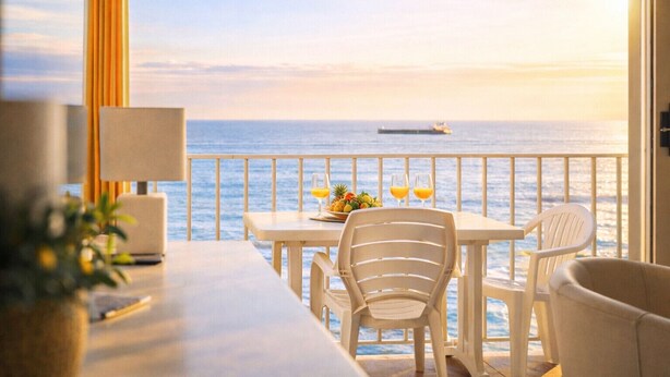 Un balcón con vistas al mar, una mesa con sillas y un frutero.