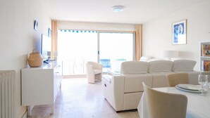 Una sala de estar moderna y bien iluminada con un sofá, sillas, una mesa de comedor y vistas a través de un gran ventanal.