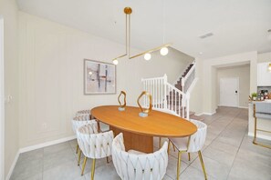 A dining area with a round wooden table, white upholstered chairs, and a modern chandelier.