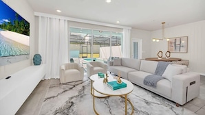 Ein modernes Wohnzimmer mit einem weißen Sofa, einem Couchtisch und Blick auf Pool und Strand durch große Fenster.