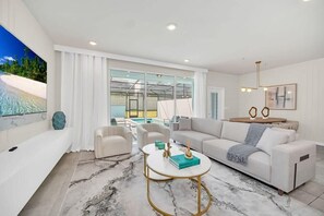 A modern living room with a white sofa, a coffee table, and a view of a pool and beach through large windows.