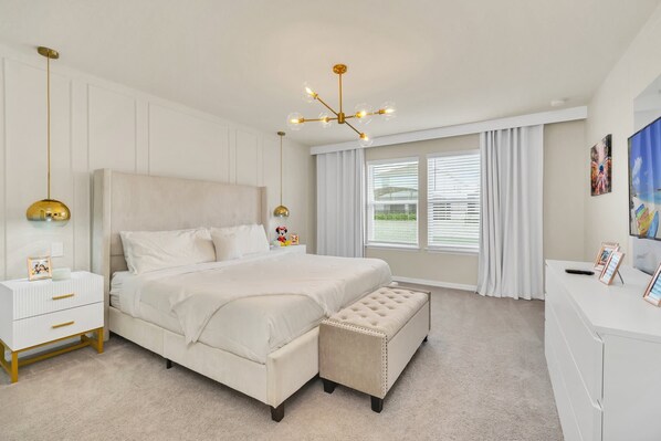 A bedroom with a large bed, bedside tables, a bench, a desk, and a window with curtains.