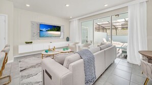 Ein modernes Wohnzimmer mit großem Fernseher, bequemen Sitzgelegenheiten, einem Balkon mit Aussicht und einem klaren, minimalistischen Design.