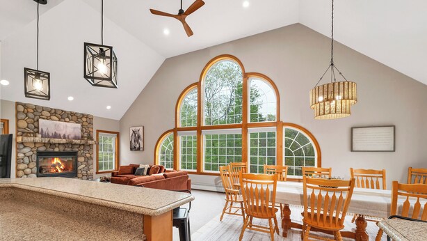 A spacious kitchen with a stone fireplace, large windows, and a dining area with wooden chairs and a table.