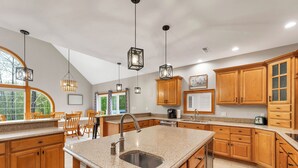 A kitchen with wooden cabinets, granite countertops, a large island with a sink, pendant lighting, and a view of the outdoors.