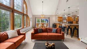 A spacious living room with a large window, a dining area, and a kitchen with bar stools.