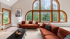 A spacious living room with a large arched window, a brown sofa, a coffee table, and a framed artwork on the wall.