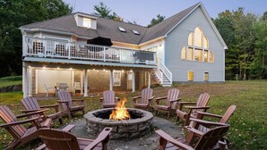 A two-story house with a fire pit in the backyard, surrounded by Adirondack chairs.