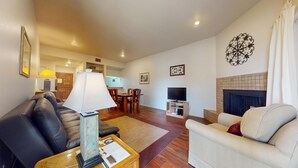A living room with a sofa, armchair, coffee table, TV, fireplace, and a dining area with chairs and a table. - River City Resorts: B115 : Free Tubes with Rental! (New Braunfels)