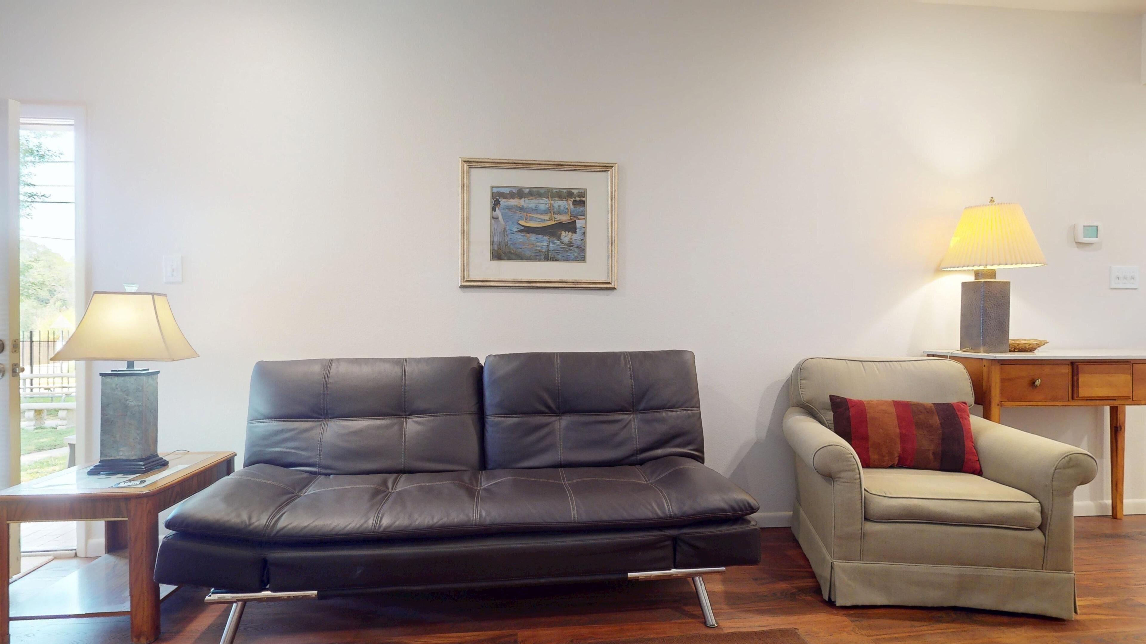 A living room with a black leather sofa, a beige armchair, a wooden coffee table, and two lamps.
