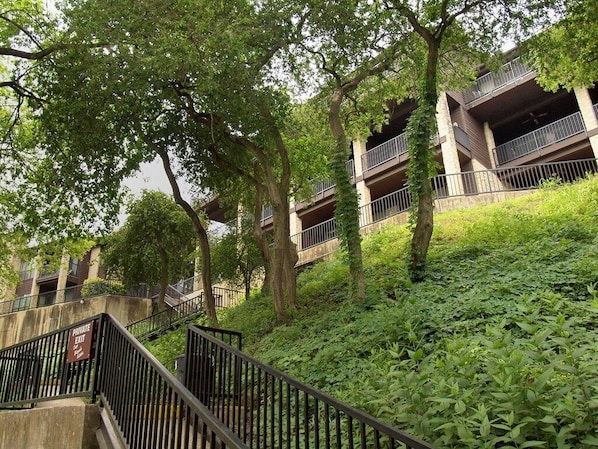 A multi-story building with balconies, surrounded by lush greenery and trees.