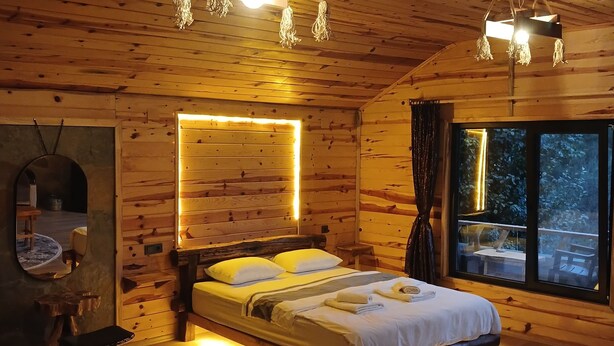 Camera da letto di un accogliente chalet in legno, con un letto grande, lampade sui comodini e vista dalla finestra.