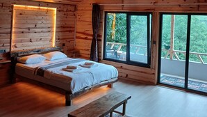 Camera da letto in una baita di legno, con un letto, una panca e ampie finestre.