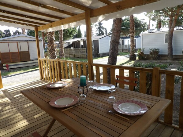 Une terrasse en bois avec une table dressée pour deux personnes, donnant sur un quartier résidentiel composé de maisons mobiles.