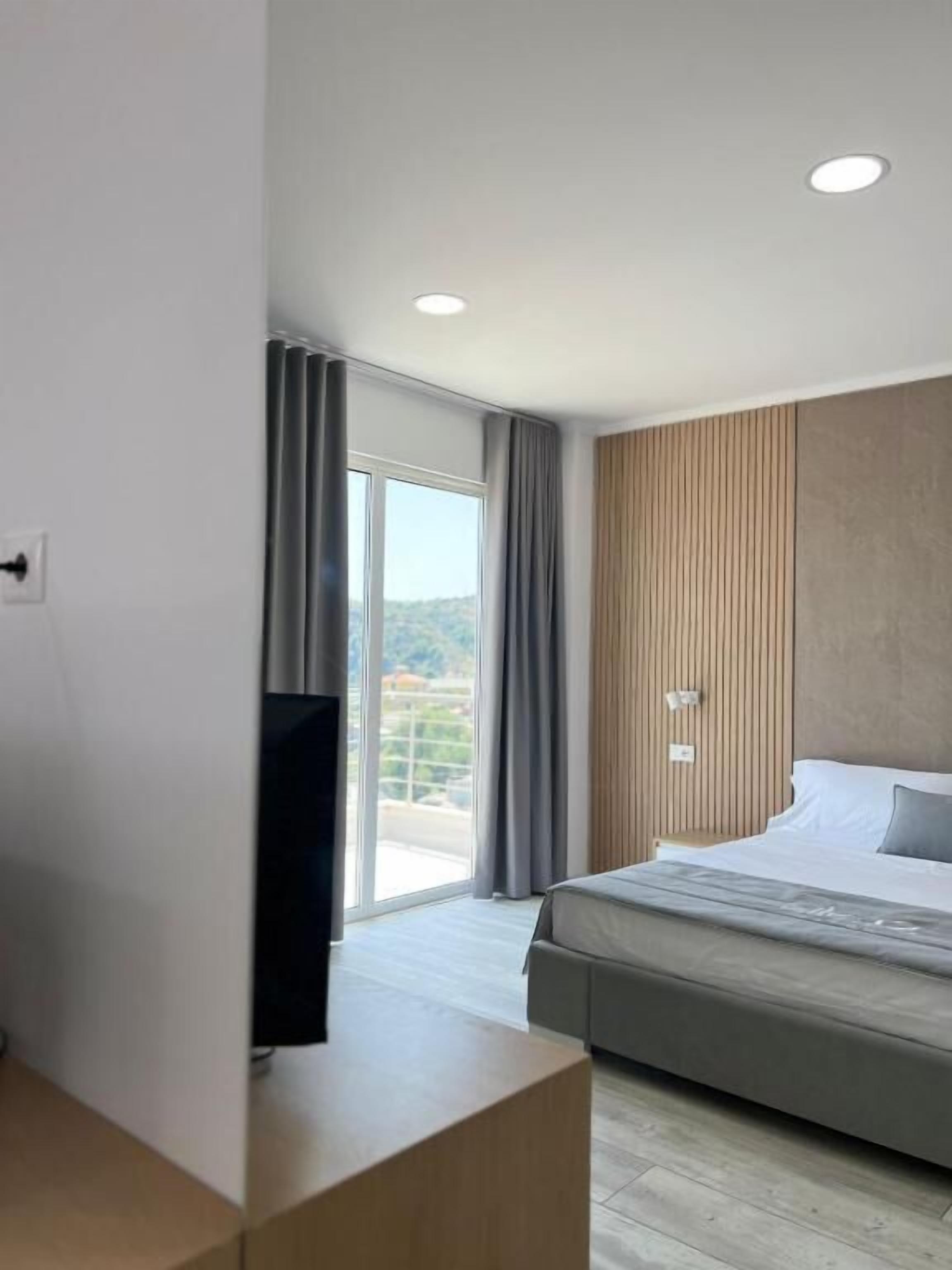 A modern hotel room with a large bed, a flat-screen TV, and a balcony with a view of the city.