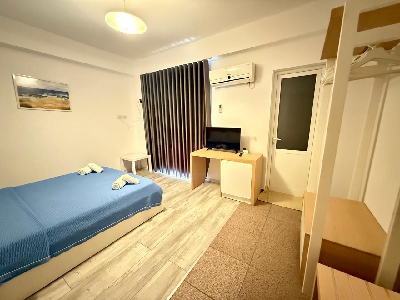 Quarto de hotel com cama, escrivaninha, televisão e aparelho de ar condicionado.