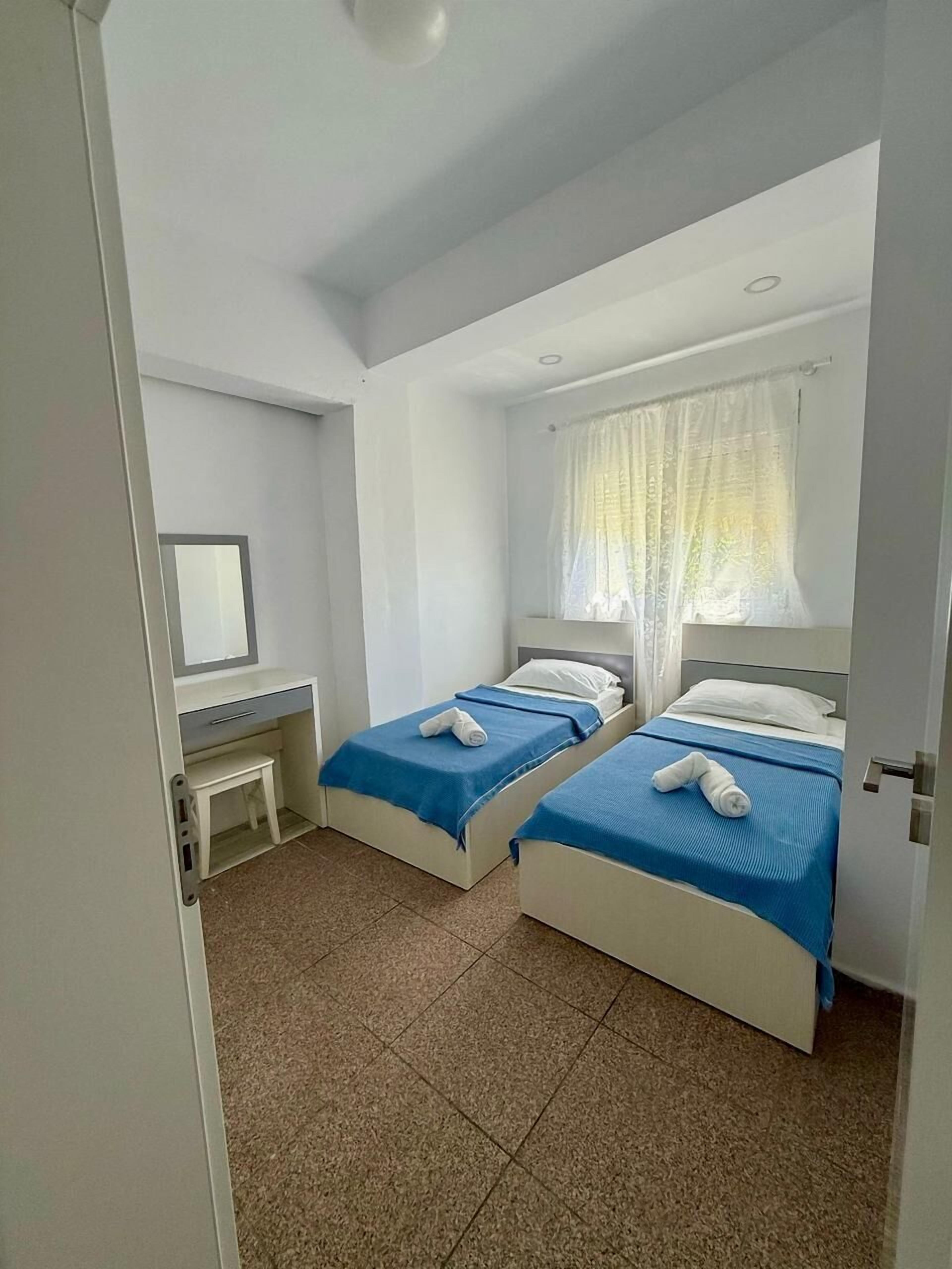 A room with two beds, a desk, and a window with curtains.