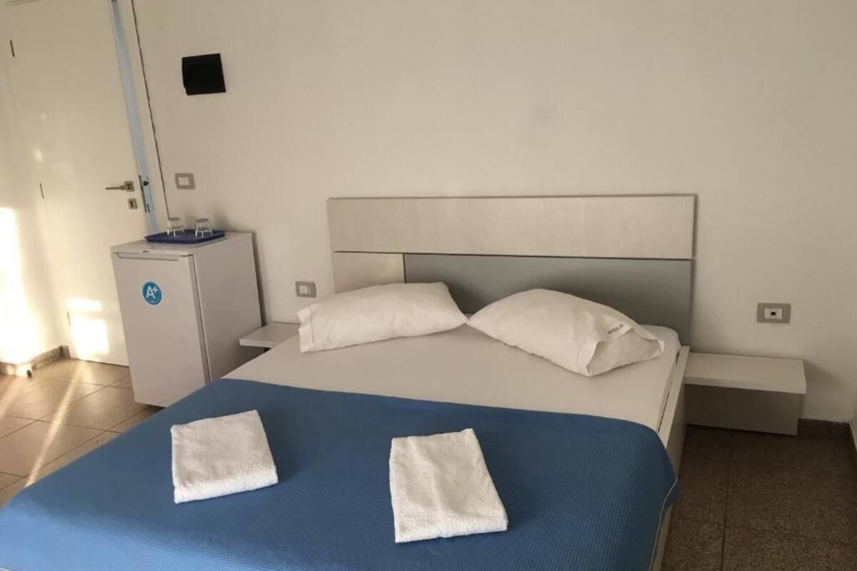 A hotel room with a bed, two white pillows, a blue bedspread, and two white towels on the bed.