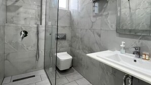 A modern bathroom with a glass-enclosed shower, a white sink, and a marble-tiled wall. - Hotel Stolis (Himarë)