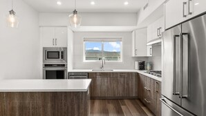 A modern kitchen with a central island, stainless steel appliances, and a view of the outdoors. - The Central | Downtown + Rooftop Patio (Kelowna)