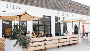 An outdoor seating area with wooden benches and umbrellas in front of a building labeled "BREAD" and "SPROUT COFFEE". - The Central | Downtown + Rooftop Patio (Kelowna)