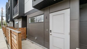 A modern building with a grey facade, a white door, and a balcony. - The Central | Downtown + Rooftop Patio (Kelowna)