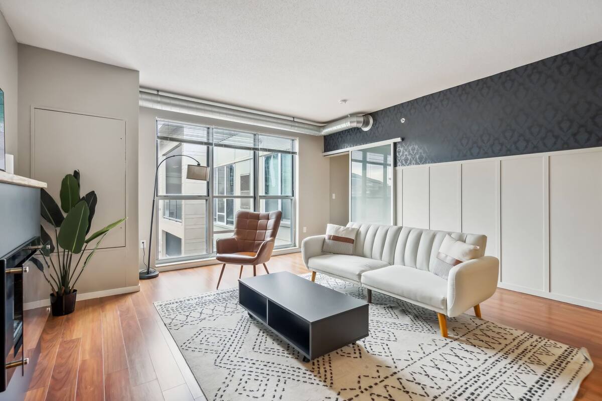 Un salon moderne avec un canapé, une table basse, un fauteuil et une grande fenêtre.