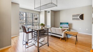 Een moderne keuken met een groot raam, een eethoek met een tafel en stoelen, en een televisie aan de muur.