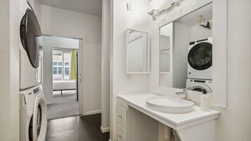 A modern bathroom with a large mirror, a sink, and a washing machine.