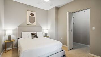 Una habitación de hotel con cama, lámparas de noche, ventilador de techo y una puerta.