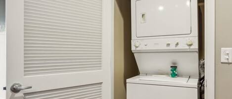 A laundry room with a white dryer and a closed door with horizontal slats.