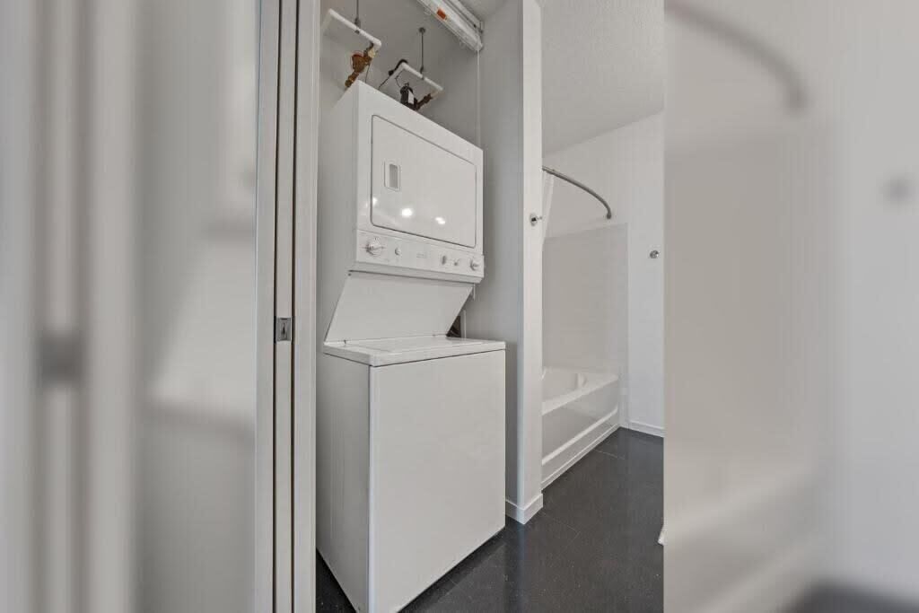 A compact laundry area with a washer and dryer, a small shelf with items, and a shower area.