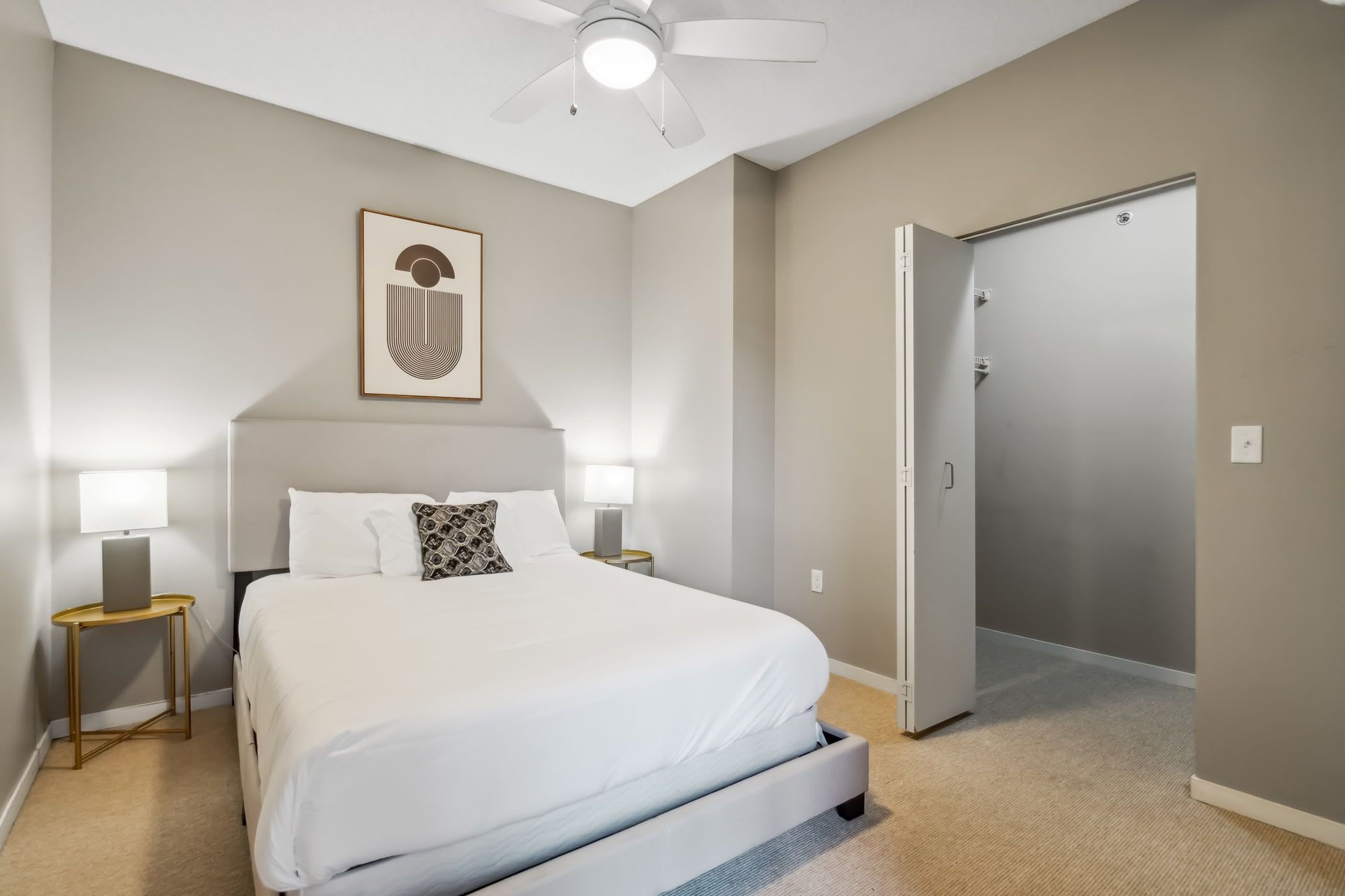 Une chambre à coucher avec un lit, des lampes de chevet, un ventilateur de plafond, une porte et un tableau encadré au mur.