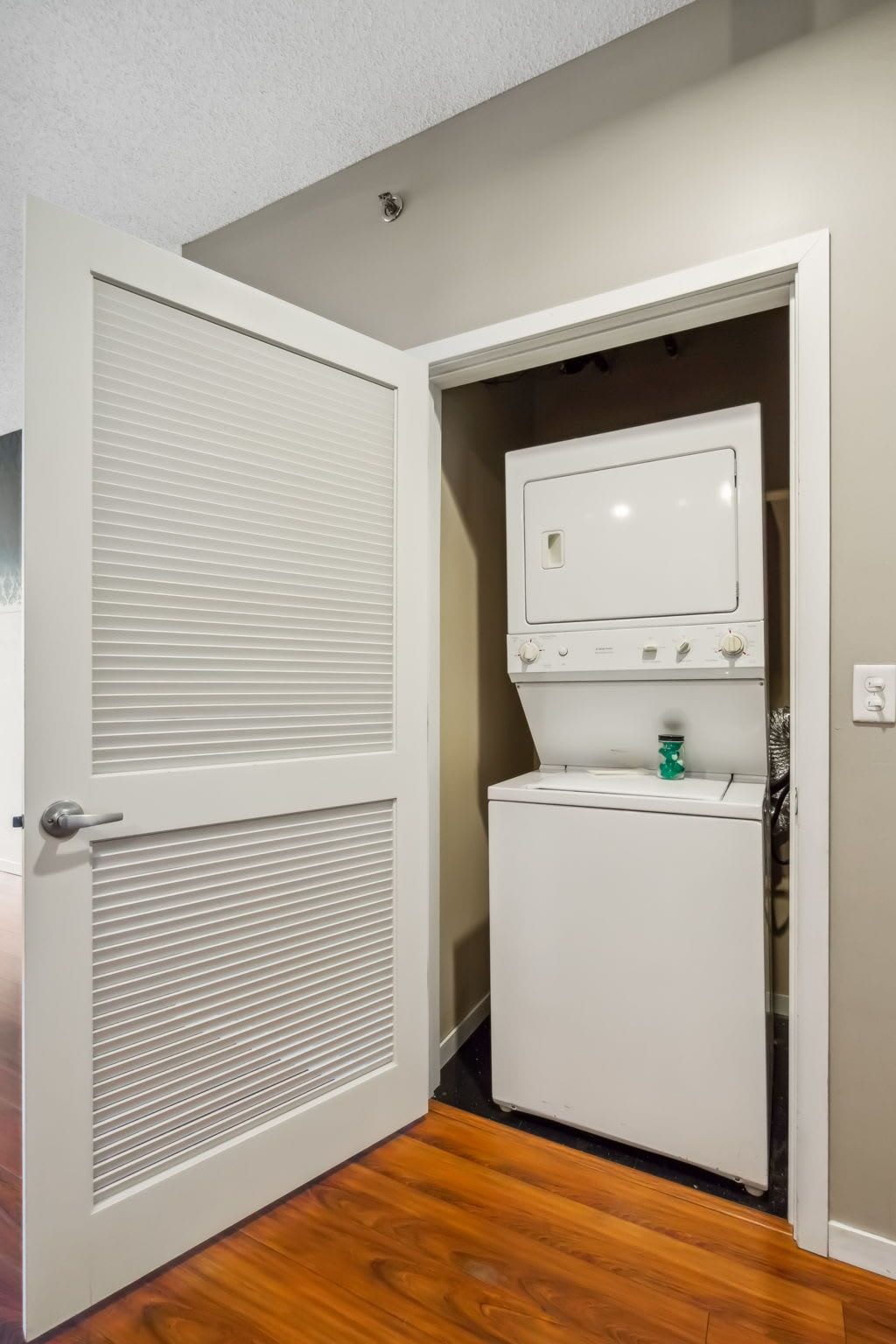 Una sala de bugaderia amb una rentadora i una assecadora blanques, una porta amb finestre i un interruptor de llum a la paret.