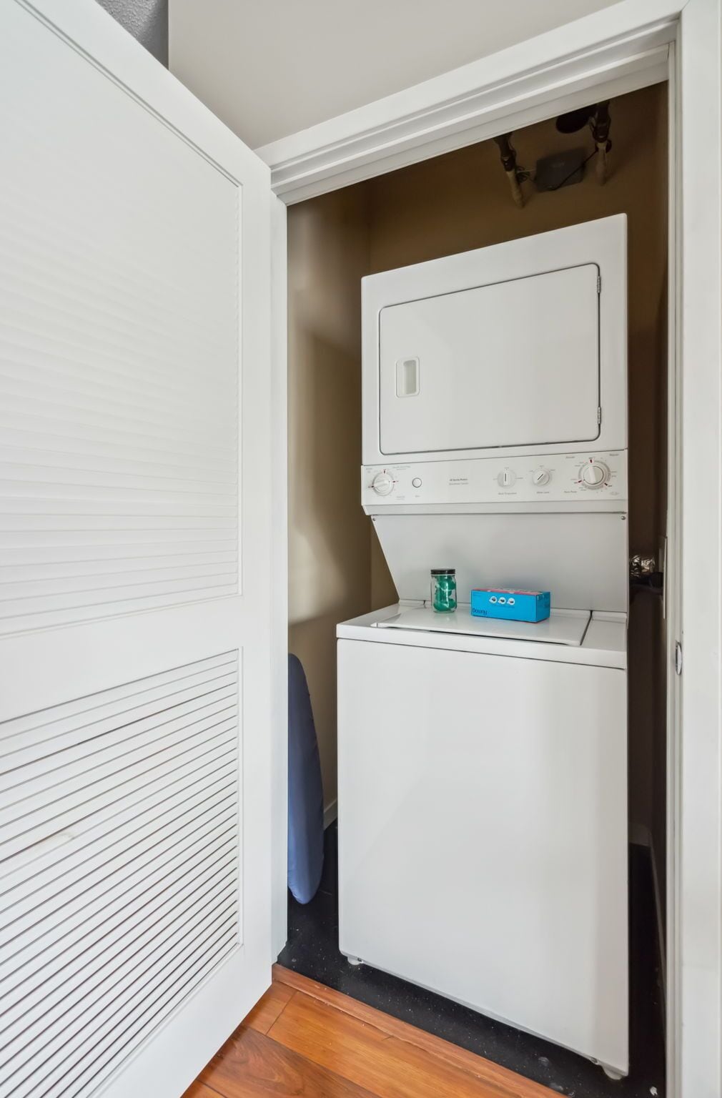 A compact laundry room with a front-loading washer and dryer, a small storage cabinet, and a vented cabinet door.