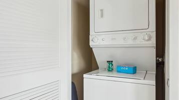 A compact laundry room with a front-loading washer and dryer, a small storage cabinet, and a vented cabinet door.